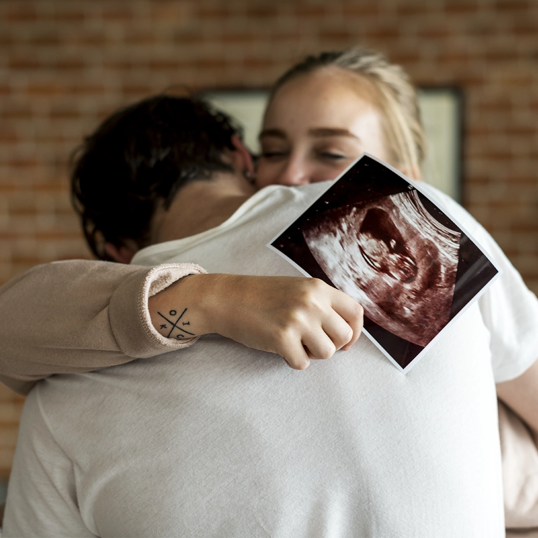 A Woman Holding An Ultrasound Image Result Of Future Baby Hugging Her Husband