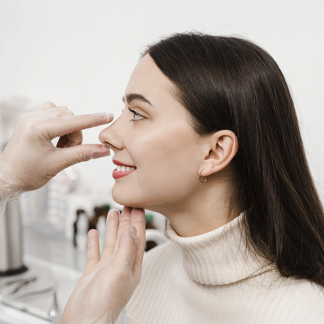 The Side View Of A Young Woman Is Seen With Her Nose Is Being Examined By The Surgeon