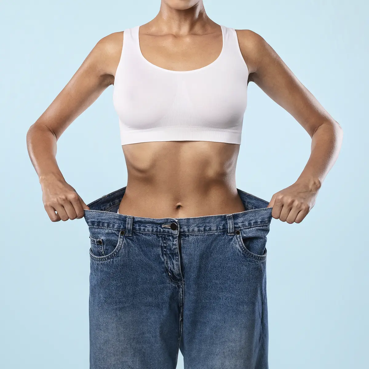 A Young Woman After Surgery Holding The Sides Of Her Jeans Showing The Weight She Has Lost
